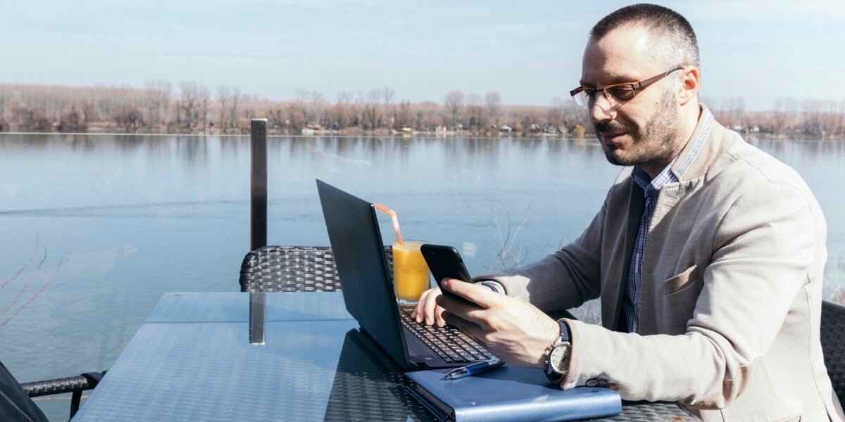 Developer using smartphone and laptop near water